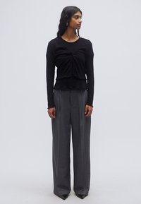 Μαύρο ριπ μακρυμάνικο τοπ με δετή λεπτομέρεια μπροστά, σε συνδυασμό με φαρδιά γκρι παντελόνια με ψηλή μέση και φαρδιά μπατζάκια.