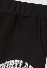 Czarne bawełniane spodnie dresowe z ribbowanym pasem, bocznymi kieszeniami oraz białą grafiką "Portland" z przodu. Gładka tekstura.