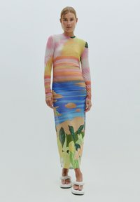 Robe à manches longues colorée avec un design de coucher de soleil dégradé en rose, jaune et bleu, présentant un imprimé floral tropical à l'ourlet.