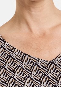 Parte superior de una prenda con un patrón geométrico en colores negro, beige y crema. El escote es redondeado y la tela tiene una textura suave.