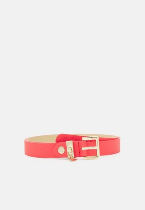 Rode leren riem met textuur, voorzien van een gesp in goudkleur en een klein hangertje, plat uitgestald tegen een grijze achtergrond.