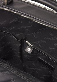 Black leather bag interior features a zippered pocket and a fabric lining with repeating logo pattern. Silver hardware and smooth texture.