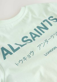 Šviesiai mėtinės spalvos medvilninė marškinėliai su ryškiu tekstu "ALLSAINTS" ir papildomais simboliais, atspausdintais tamsiai žalia spalva. Standartinio apvalaus kaklo dizainas.