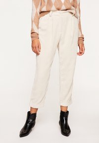 Krämfärgade kordflordbyxor med veck, med uppvikta fållar. Matchas med svarta ankelstövlar som förstärker den övergripande texturerade stilen.