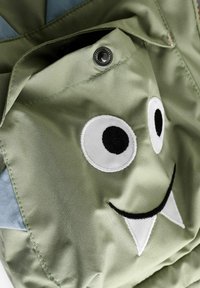 Tissu vert avec un design de visage de monstre souriant, présentant des boutons noirs, et des yeux et des dents brodés pour une texture ajoutée.