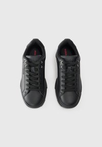 Black leather sneakers with a textured finish, featuring flat laces, silver eyelets, and a red logo on the black insole. Classic low-top design.