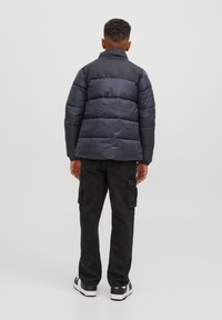 Mornarsko modra podložena jakna s horizontalnimi prešitimi sekcijami, visok ovratnik, oblečena čez črne cargo hlače in bele superge.