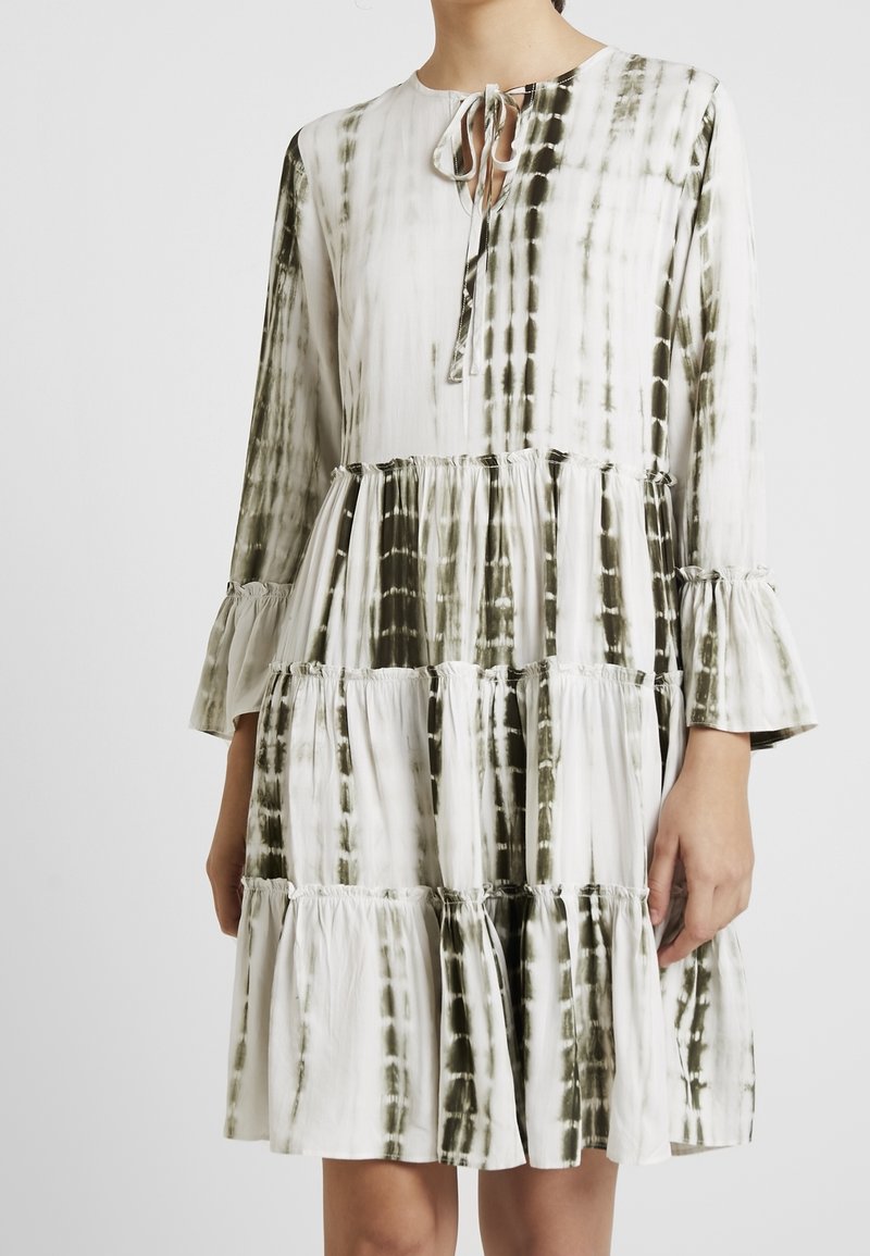 Långärmad klänning med en blandning av vita och olivgröna tie-dye-mönster, med volanger och en nyckelhålsringning med knytdetalj.