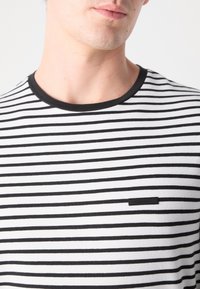 T-shirt à manches courtes en blanc avec des rayures horizontales noires, doté d'un col rond côtelé noir et d'une petite étiquette de marque sur la poitrine.