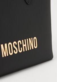 Zwarte neplederen tas met een gouden "MOSCHINO" logo aan de onderkant. Strak ontwerp met een gladde textuur en minimale detailing.