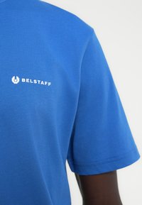 Μπλε βαμβακερό T-shirt με κοντά μανίκια και στρογγυλή λαιμόκοψη. Λογότυπο «BELSTAFF» σε λευκό στην αριστερή πλευρά του στήθους. Ομαλή υφή.