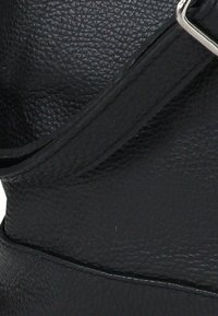 Black textured leather handbag featuring a wide strap and silver hardware accents. The surface shows a pebbled pattern and smooth stitching.