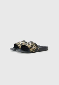 Sorte sandaler med bred reim som har et gult abstrakt mønster. Sålen er glatt og flat, designet for avslappet bruk.