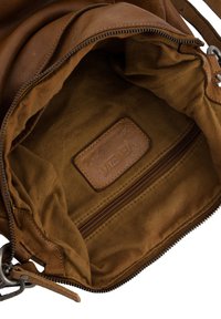 Intérieur d'un sac à main en cuir marron avec une texture douce, comprenant une poche zippée et une étiquette en cuir de marque. La doublure est en tissu tanné clair.