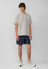 T-shirt oversized beige clair, shorts en denim courts, et baskets neutres. Tissu lisse avec une coupe décontractée. Manches courtes et design simple.