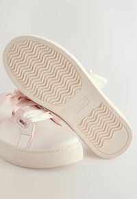 Baskets roses avec des lacets en satin, semelle en caoutchouc texturée et tige en synthétique lisse. Présente un motif ondulé sur la semelle extérieure.