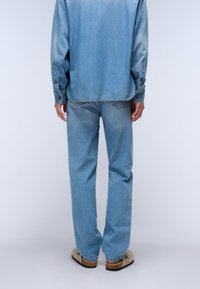 Conjunto de denim que incluye una camisa de botones azul clara y unos jeans rectos a juego, complementados con unos zapatos slip-on color marrón claro.