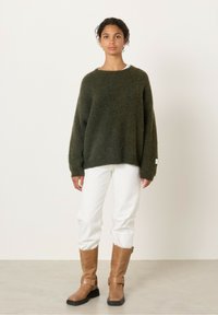 Tamsiai žalia, storesnė megzta megztinis su laisvu siluetu, derinamas su baltais, tiesaus kirpimo džinsais ir rudais, iki kelių siekiančiais batais su sagtimis.