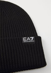 Beanie a coste nera con bordo ripiegato. Presenta un'etichetta con il marchio "EA7 EMPORIO ARMANI" in lettere bianche e grigie.