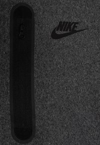 Nike šedá plsťová taška s černým zipem, texturovaným povrchem a výrazným černým logem. Jednoduchý design bez dalších akcentů.