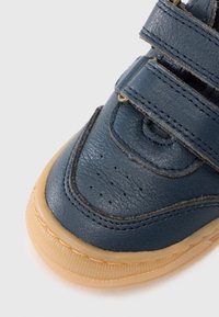 Μπλε δερμάτινο αθλητικό παπούτσι με τρεις λουριά με βέλκρο, διάτρητο πάνω μέρος και σόλα από καουτσούκ χρώματος καραμέλας. Κοντινή λήψη που αναδεικνύει την υφή και την αντίθεση των χρωμάτων.