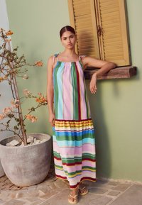 Maxi dress with multicolored vertical stripes in pink, green, blue, and yellow. Fabric is lightweight. Features adjustable tie straps and a ruffled hem.