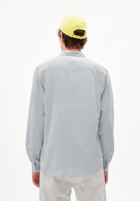 Lichtgrijs langmouwen shirt met een kraag en knoopmanchetten, gemaakt van een glad materiaal. Gecombineerd met een heldergele pet.