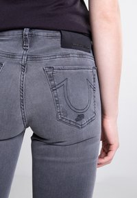 Szare dżinsy denimowe o dopasowanym kroju, z naszytym logo na tylnej kieszeni i czarną skórzaną metką na pasku.