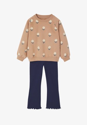 Beige long-sleeve sweater with white flower patterns paired with dark blue ribbed pants with ruffled hems.