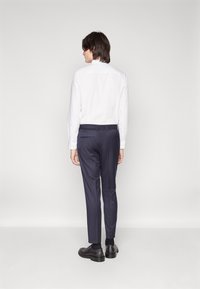 White long-sleeve shirt with buttons, paired with navy trousers featuring a stretchy waistband. Black shoes and socks complete the outfit.