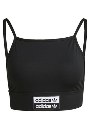 Nainen, jolla on musta lyhyt Adidas-toppi, musta nahkatakki, ylös käärityt korkeavyötäröiset siniset farkut ja valkoiset Adidas-tossut mustilla raidoilla.