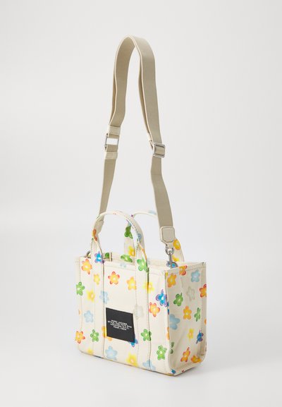 Canvasväska med färgglad blommönster, ljus bakgrund, dubbla handtag upptill, justerbar beige axelrem och svart rektangulär logotyp.