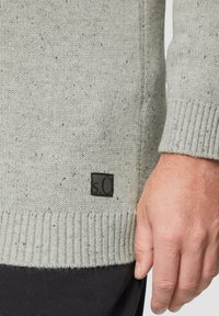 Helles Graues Sweatshirt mit strukturiertem Strick, mit einem gerippten Saum. Ein schwarzes Etikett mit "s.O" ist unten links sichtbar.