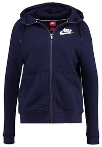 Námořnická modrá mikina na zip s klokankou, kapucí na šňůrku a bílým logem Nike na hrudi. Vyrobeno z měkké, texturované látky.