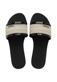 Musta sandaalit, joissa on kudottu vaalean beige vyö herringbone-kuviolla ja kiiltävät mustat yksityiskohdat. Rakeinen pohja tarjoaa pidon ja mukavuutta.