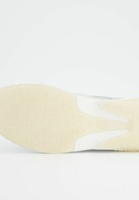 Tenisky s strukturovaným bílým svrškem, měkkou krémovou gumovou podrážkou a výrazným designem podrážky s vlnitým vzorem. Minimalistické viditelné švy.