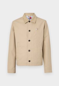 Beige bomullsjakke med krage, frontknapper og sidelommer. Har et lite emblem på brystet og stripete innfôr.