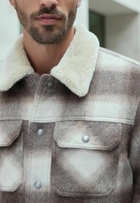 Brown and cream checkered wool jacket with a soft fleece collar, featuring silver snap buttons and two front pockets.