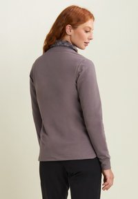 Maglietta grigia a maniche lunghe con colletto alto, caratterizzata da un interno testo. Il materiale sembra morbido ed elastico, con un design aderente.