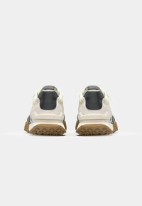 Pogled straga na bijele i sive sportske cipele s teksturiranim gumenim potplatom i crnim prugastim detaljima. Imaju jastučićasti ovratnik i brendirani detalj.