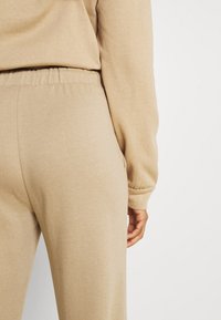 Beige sweatpants med elastisk midja och sidofickor, med en mjuk textur och avslappnad passform, kompletterad med en långärmad topp.