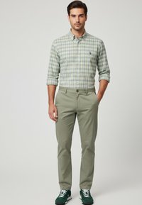 Camisa de cuadros en verde, azul y blanco; pantalones caqui; zapatillas verdes; ajuste casual; textura notable en la tela.