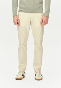 Beige lige bukser med en glat tekstur, parret med hvide sneakers med sorte striber. Toppen er en lys grå langærmet.