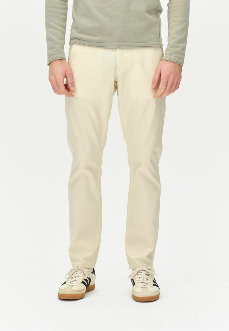 Beige lige bukser med en glat tekstur, parret med hvide sneakers med sorte striber. Toppen er en lys grå langærmet.