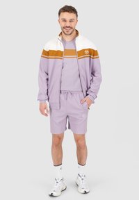 lavender athletic tracksuit with white and brown stripes, zip jacket, matching shorts, lightweight fabric, logo on chest and shorts, paired with white sneakers.