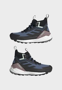 Deux chaussures de trail montantes Adidas Terrex noires et bleues avec des semelles intermédiaires blanches amortissantes et des semelles extérieures robustes vues de profil.