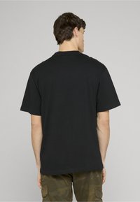 Černé bavlněné tričko s krátkými rukávy, kulatým výstřihem a volnějším střihem. Zadní strana je jednobarevná bez viditelných log nebo vzorů.