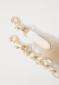 Gold-tone metal clips attached to a beige woven strap, featuring a white leather accent and large metal links.