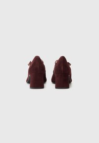 Scarpe con tacco blocco in suede bordeaux, con retro arrotondato e dettaglio alla caviglia, dotate di una suola nera liscia per stabilità e supporto.