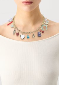 Collier en chaîne dorée avec divers pendentifs, y compris un cœur, une plume et une pierre précieuse en bleu, rouge et argent, présenté sur un haut clair.